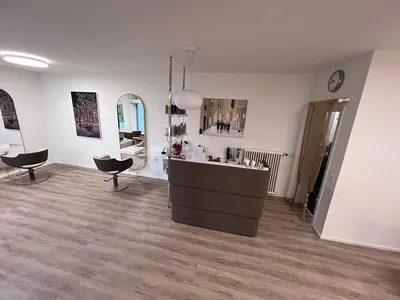 Blick in den Salon mit Empfangstheke, runden Spiegeln und Bedienstühlen