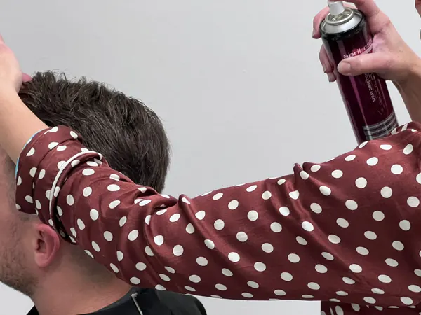 Coiffeuse fixiert die Frisur eines Kunden mit Haarspray